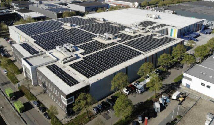 Luchtfoto van het bedrijfspand van Wilco in Amersfoort, met op het platte dak volledig belegd met zonnepanelen en op de voorgrond geparkeerde voertuigen en bedrijfswagens.